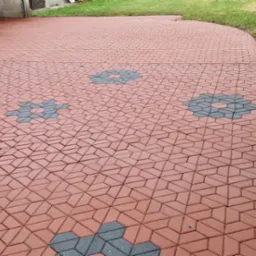 Czerwona kostka brukowa ułożona we wzór z szarymi akcentami w kształcie kwiatów, prowadząca od bramy garażowej przez trawnik, po świeżym czyszczeniu.