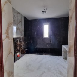 Complex - Nowoczesna łazienka z marmurowymi płytkami w odcieniach bieli i brązu, ciemna ściana z oknem, widok zza framugi drzwi. Minimalistyczny design.