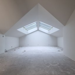 Complex - Wnętrze poddasza po malowaniu na biało, z dwoma oknami dachowymi w trójkątnej wnęce. Surowa podłoga, ściany świeżo pomalowane, widoczne instalacje elektryczne.