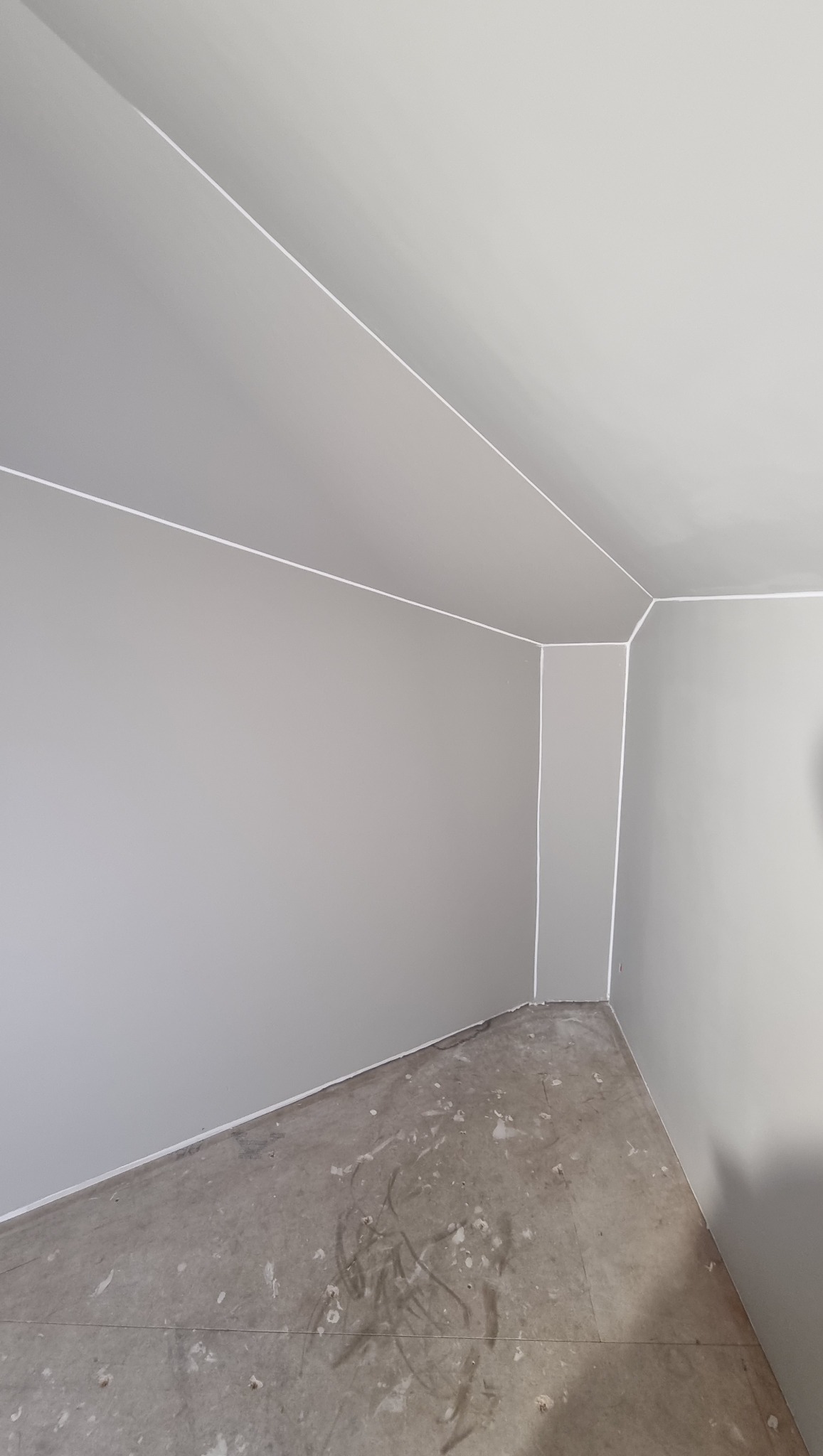 Szare wnętrze po malowaniu z widocznymi białymi liniami oddzielającymi ściany od sufitu i podłogi. Na podłodze widoczne ślady farby.
