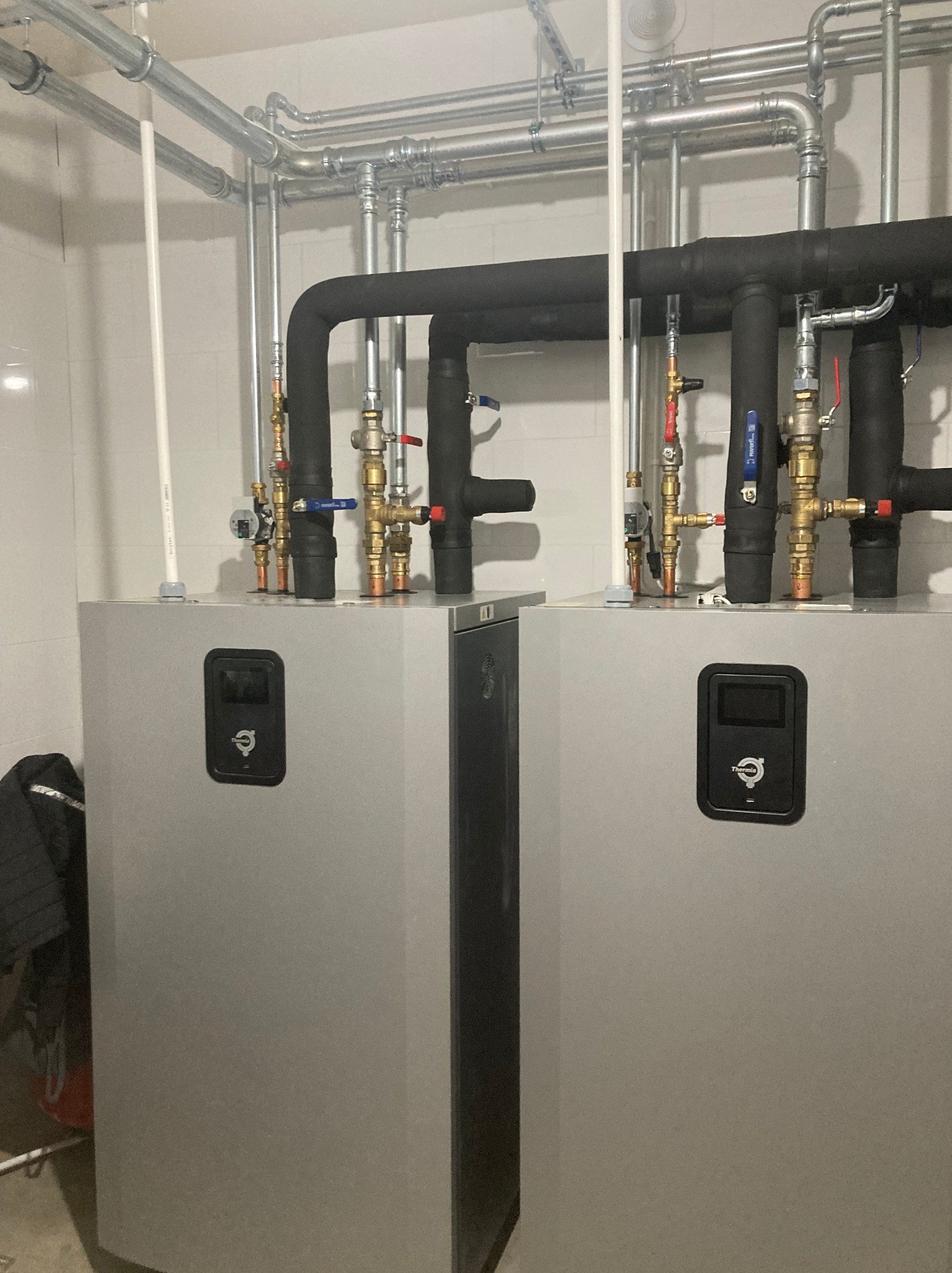 Dwie szare pompy ciepła Thermia z rurami w tle, zainstalowane w Sobótce. Widoczne liczne zawory i izolacje termiczne na rurach.