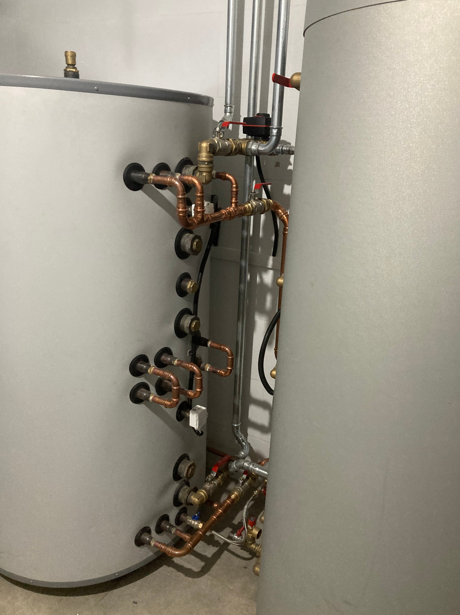 Szare zbiorniki z miedzianą instalacją hydrauliczną i zaworami. Widoczne liczne przyłącza i rury. Elementy instalacji grzewczej w kotłowni.