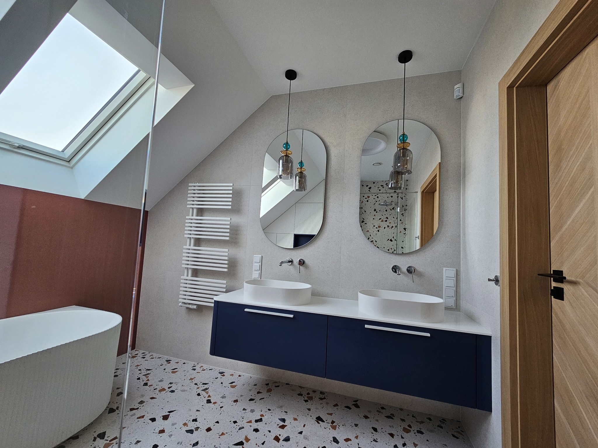 Stylowa łazienka na poddaszu w Krakowie z dwoma umywalkami nablatowymi, wiszącą szafką w kolorze granatowym i lustrami w kształcie łezki. Widoczna wanna i grzejnik.
