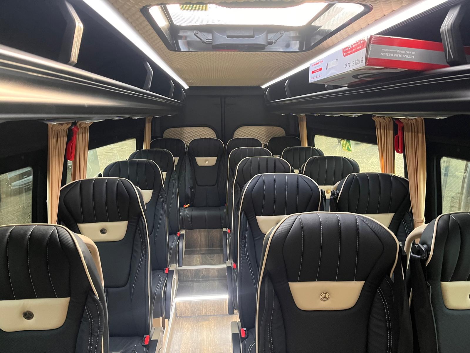 Wnętrze luksusowego busa marki Mercedes z czarnymi skórzanymi fotelami, beżowymi wstawkami i oświetleniem LED, gotowego do komfortowego przewozu osób.
