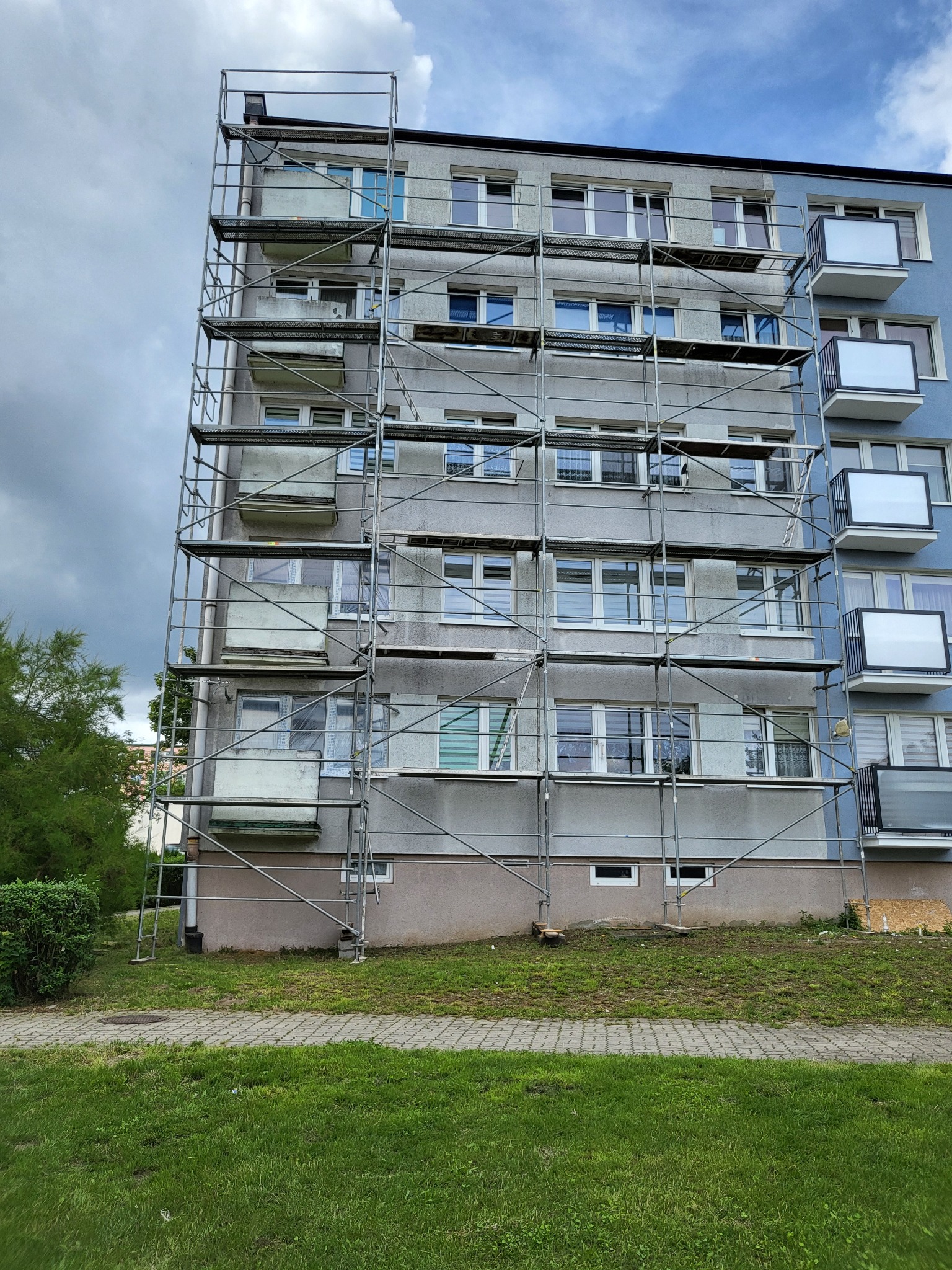 Budynek wielorodzinny w Świeciu z rusztowaniem. Przygotowania do prac elewacyjnych, widoczne balkony i okna. Część budynku pomalowana na niebiesko.