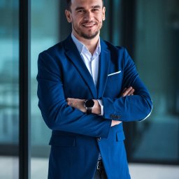 Maja Chalejew Mayove Photo - Uśmiechnięty mężczyzna w błękitnej marynarce, z zegarkiem na ręku, pozuje na tle szklanej ściany we Wrocławiu. Zdjęcie biznesowe.