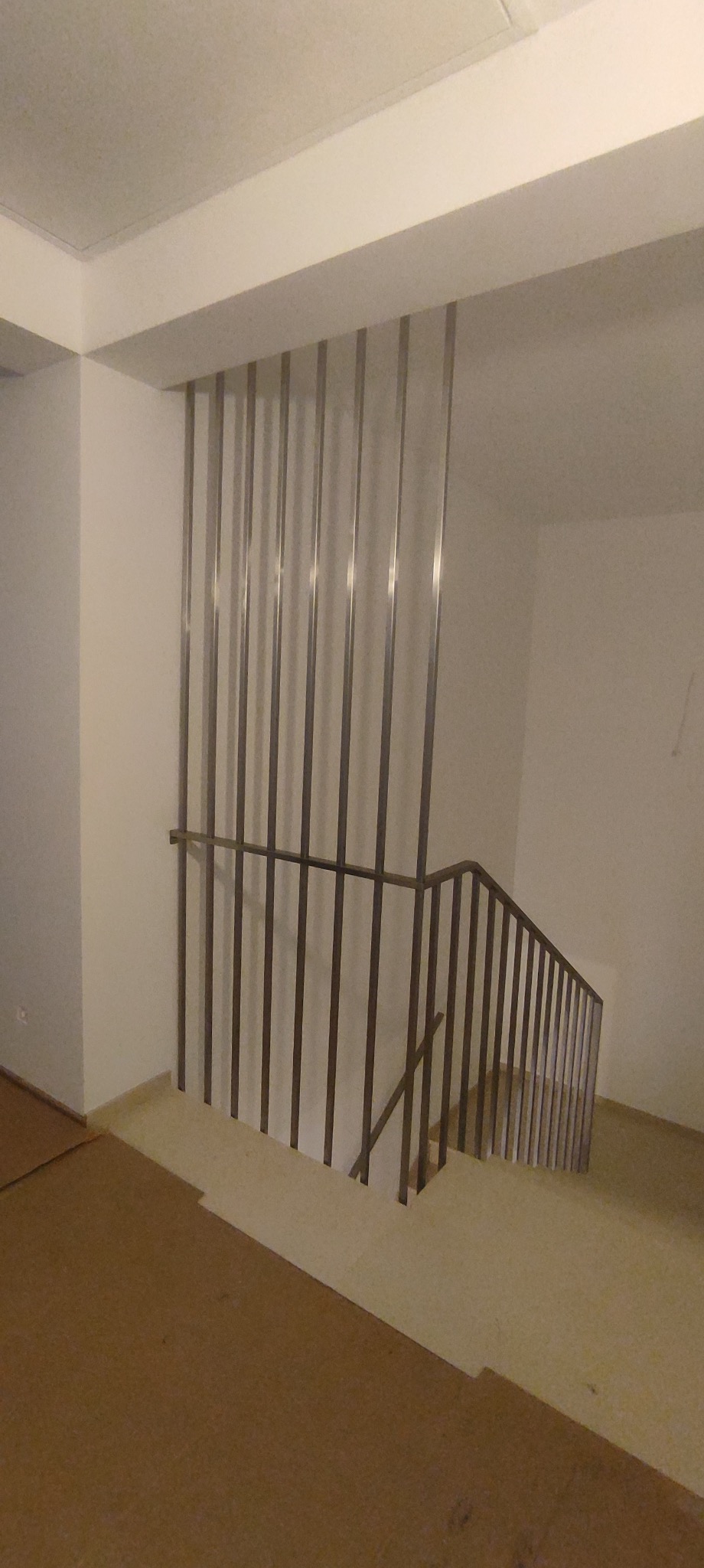 Minimalistyczna balustrada schodowa z pionowych, metalowych prętów, tworząca nowoczesny akcent w jasnym wnętrzu. Ujęcie z dołu, podkreślające geometrię konstrukcji.