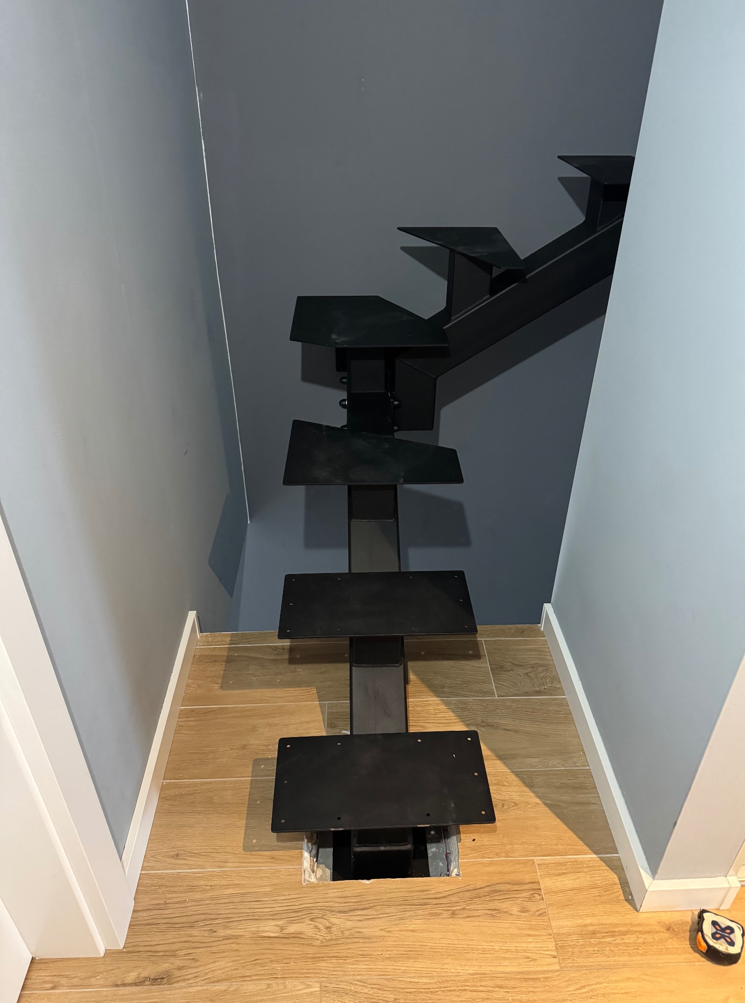 Wnętrze z montowanymi schodami metalowymi o nowoczesnej, ażurowej konstrukcji. Widoczne mocowania do podłogi i częściowo zamontowane stopnie.