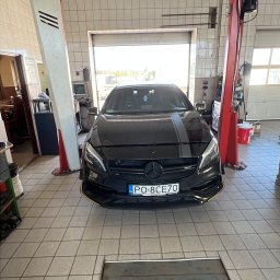 S.R Serwis Szymon Rutkowski - Czarny Mercedes A-klasa z szarym pasem na masce, zaparkowany w warsztacie z podnośnikiem i kanałem. Widok z przodu na tle otwartej bramy garażowej.