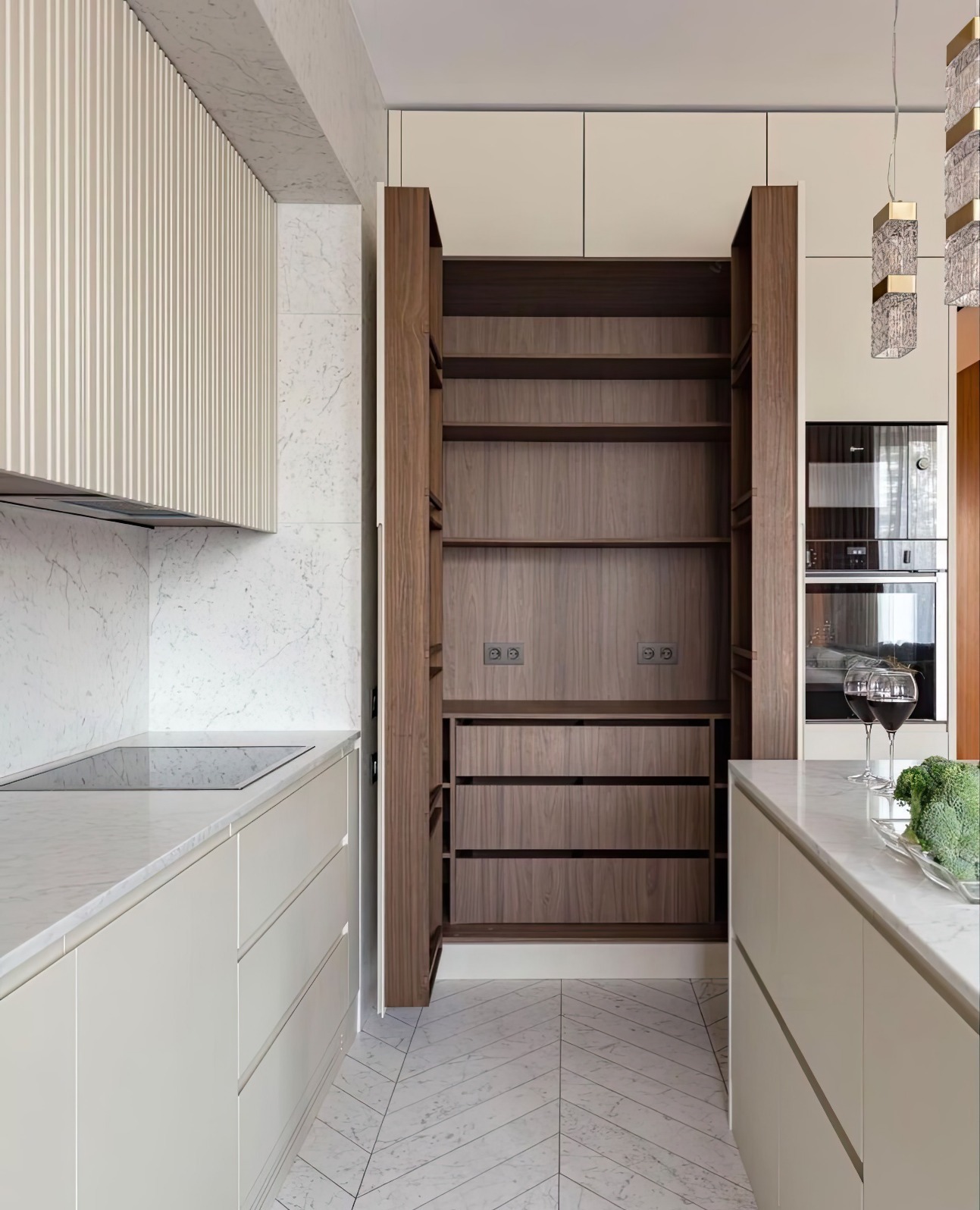Nowoczesna kuchnia z otwartą, drewnianą szafą wnękową z szufladami, marmurowym blatem i podłogą w jodełkę. Dwa kieliszki wina i brokuły na wyspie.