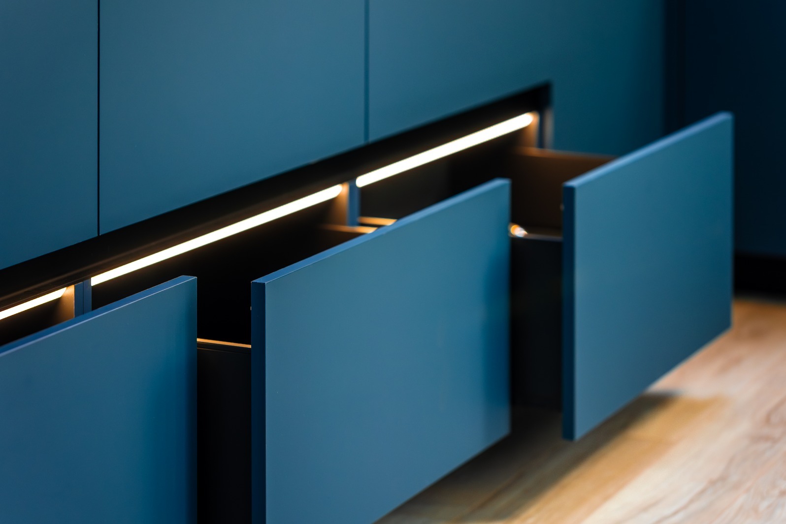 Niebieska szafka z wysuwanymi szufladami i subtelnym oświetleniem LED, ukazująca nowoczesny design i funkcjonalność mebli na wymiar.