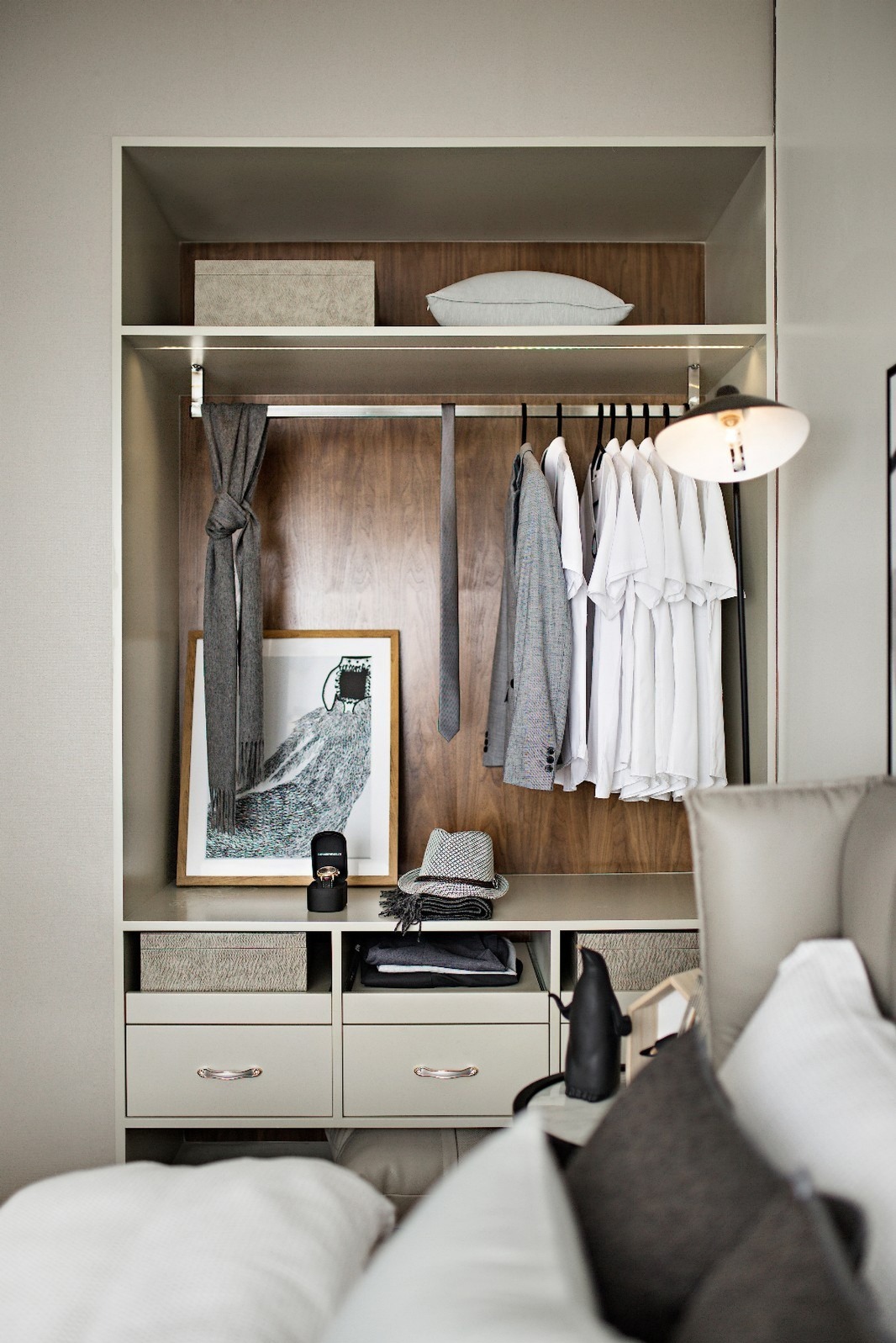 Elegancka szafa wnękowa z drewnianym panelem, oświetleniem LED i starannie dobranymi dodatkami: szal, kapelusz, grafika. Widok z perspektywy łóżka.