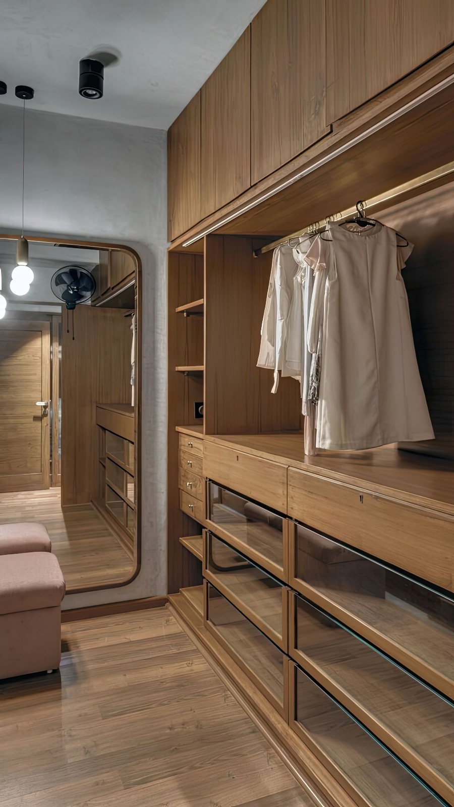 Drewniana szafa wnękowa z lustrem i oświetleniem LED. Widoczne szklane półki i wieszaki z ubraniami. Ciepłe światło podkreśla naturalny odcień drewna.