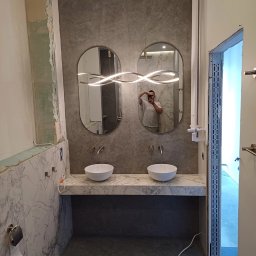 Usługi remontowe Dawid Soliński - Nowoczesna łazienka w trakcie prac: marmurowe płytki, podwójna umywalka, lustra owalne z oświetleniem LED. Widoczne niedokończone wykończenia.