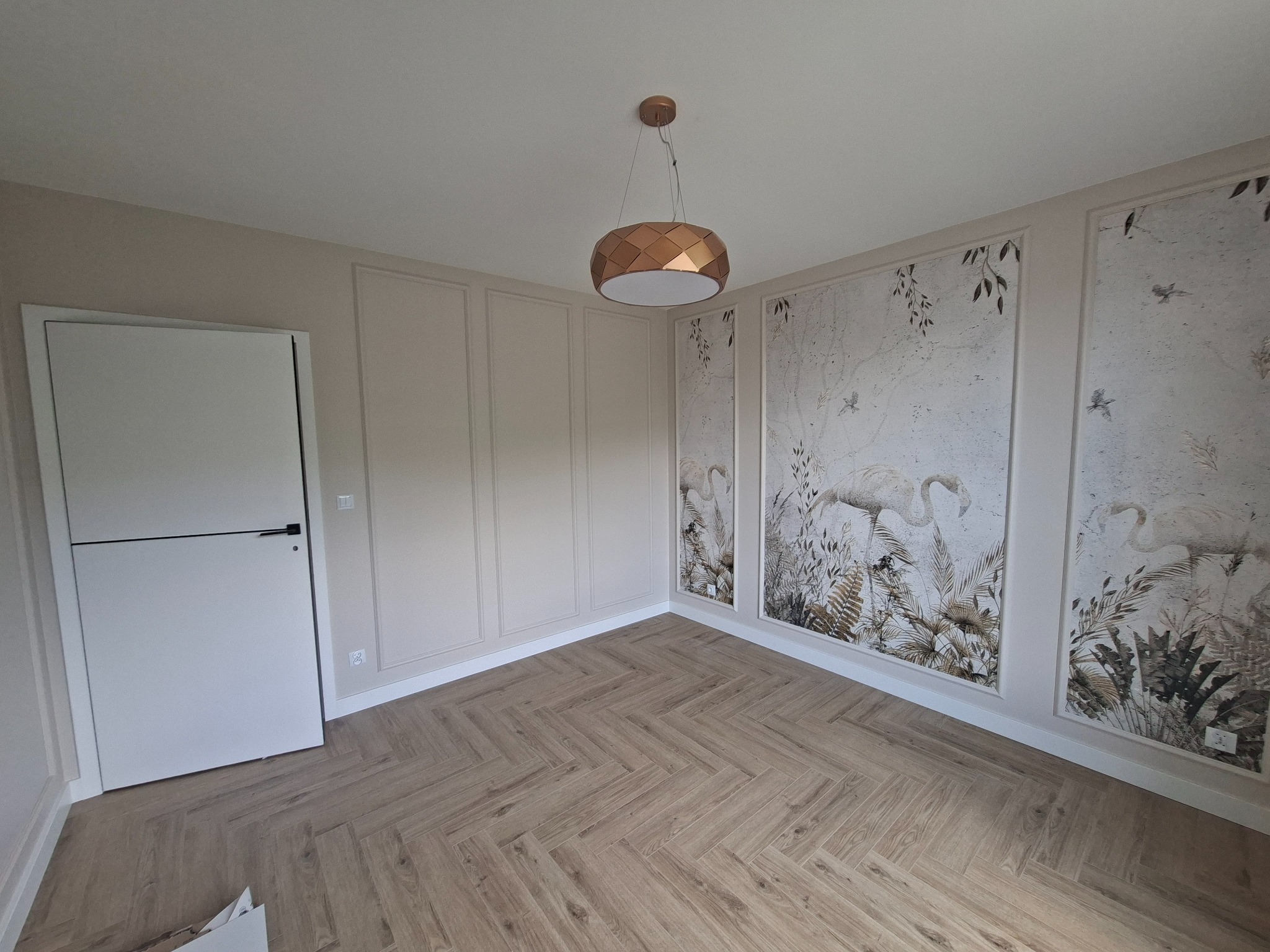 Eleganckie wykończenie wnętrza: parkiet w jodełkę, kremowe ściany z dekoracyjnymi panelami i fototapetą z motywem roślinnym. Nowoczesna lampa wisząca.