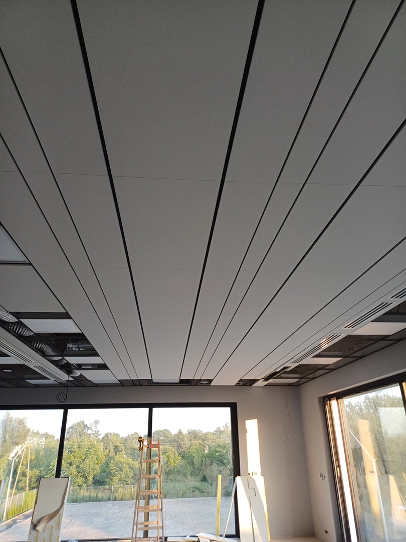 Nowoczesny sufit podwieszany z panelami i czarnymi listwami, widok z dołu, drabina w tle przy oknie, pomieszczenie w trakcie prac.