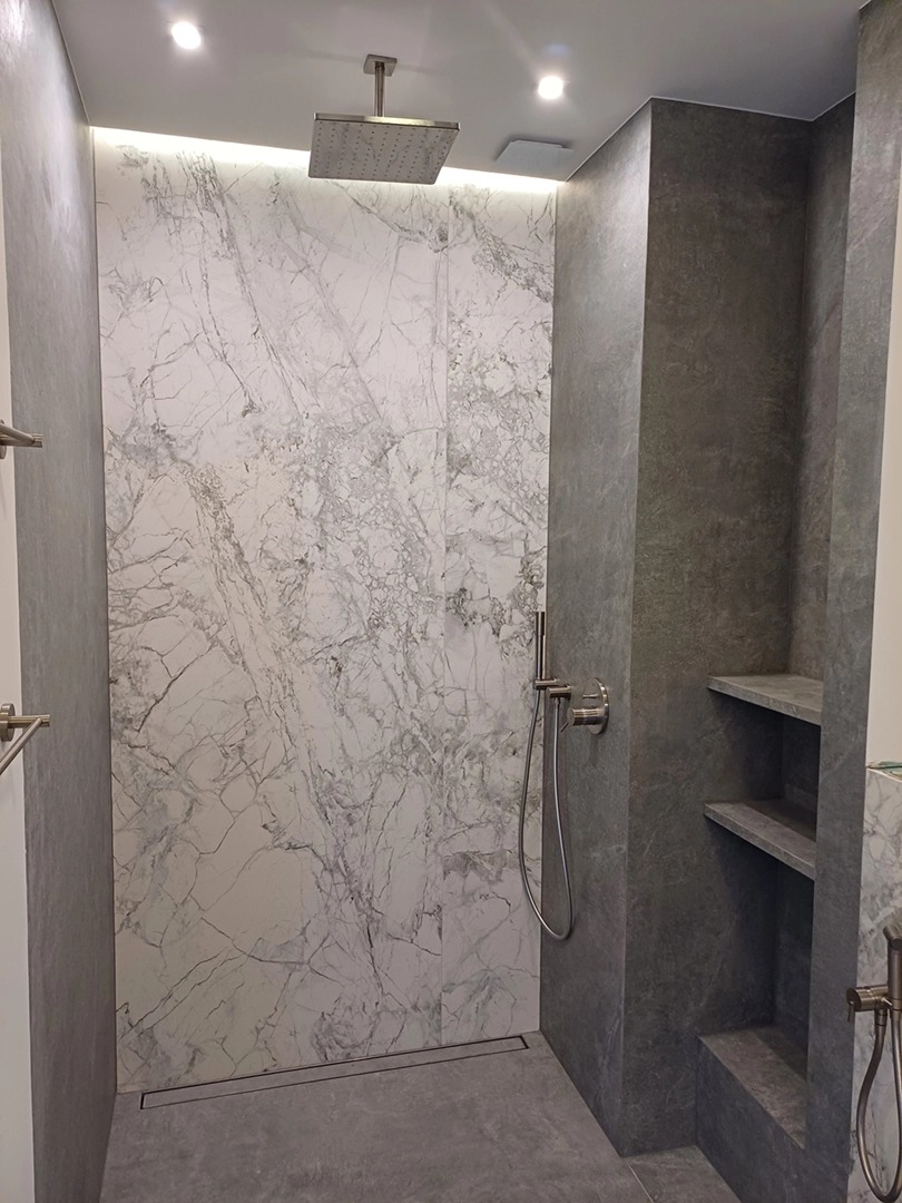 Nowoczesna kabina prysznicowa z marmurową ścianą, deszczownicą i odpływem liniowym. Szare ściany i półki wnękowe dodają elegancji.