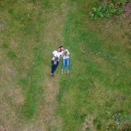 Dawid Czub - Para z psem leży na trawie, widok z góry. Kobieta trzyma bukiet polnych kwiatów. Romantyczna sesja w plenerze, naturalne światło, swobodna atmosfera.