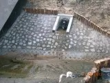 Wykończony drenaż z kamienną nawierzchnią i drewnianym obrzeżem, odprowadzający wodę do betonowego przepustu. Widok z góry.