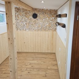 Bo Bau - Drewniane wykończenie wnętrza: boazeria, podłoga z paneli, ściana z drewnianych krążków. Widoczne drzwi do sauny i ciemne drzwi po prawej.