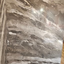 Bo Bau - Ściana z dekoracyjną, szarą farbą imitującą marmur z delikatnymi, złotymi żyłkami. Widoczny narożnik i zabezpieczenie podłogi folią malarską.