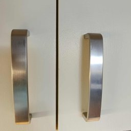 Czystonauta - Paweł Urbański - Białe fronty szafek kuchennych z metalowymi, szczotkowanymi uchwytami w kształcie litery U. Detal na czystej powierzchni po sprzątaniu.