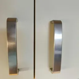 Białe fronty szafek kuchennych z metalowymi, szczotkowanymi uchwytami w kształcie litery U. Detal na czystej powierzchni po sprzątaniu.