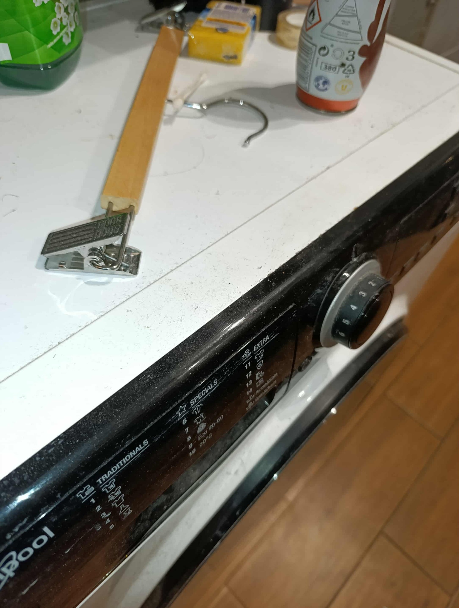 Brudna pralka Whirlpool z widocznym pokrętłem programów, obok butelka płynu, gąbka i wieszak. Widoczne zabrudzenia na powierzchni pralki.