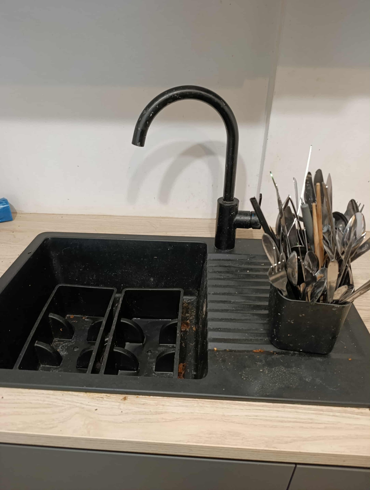 Czarny zlew z armaturą i pojemnikiem na sztućce, widoczne zabrudzenia i osady.  Ujęcie z bliska, oświetlenie naturalne.