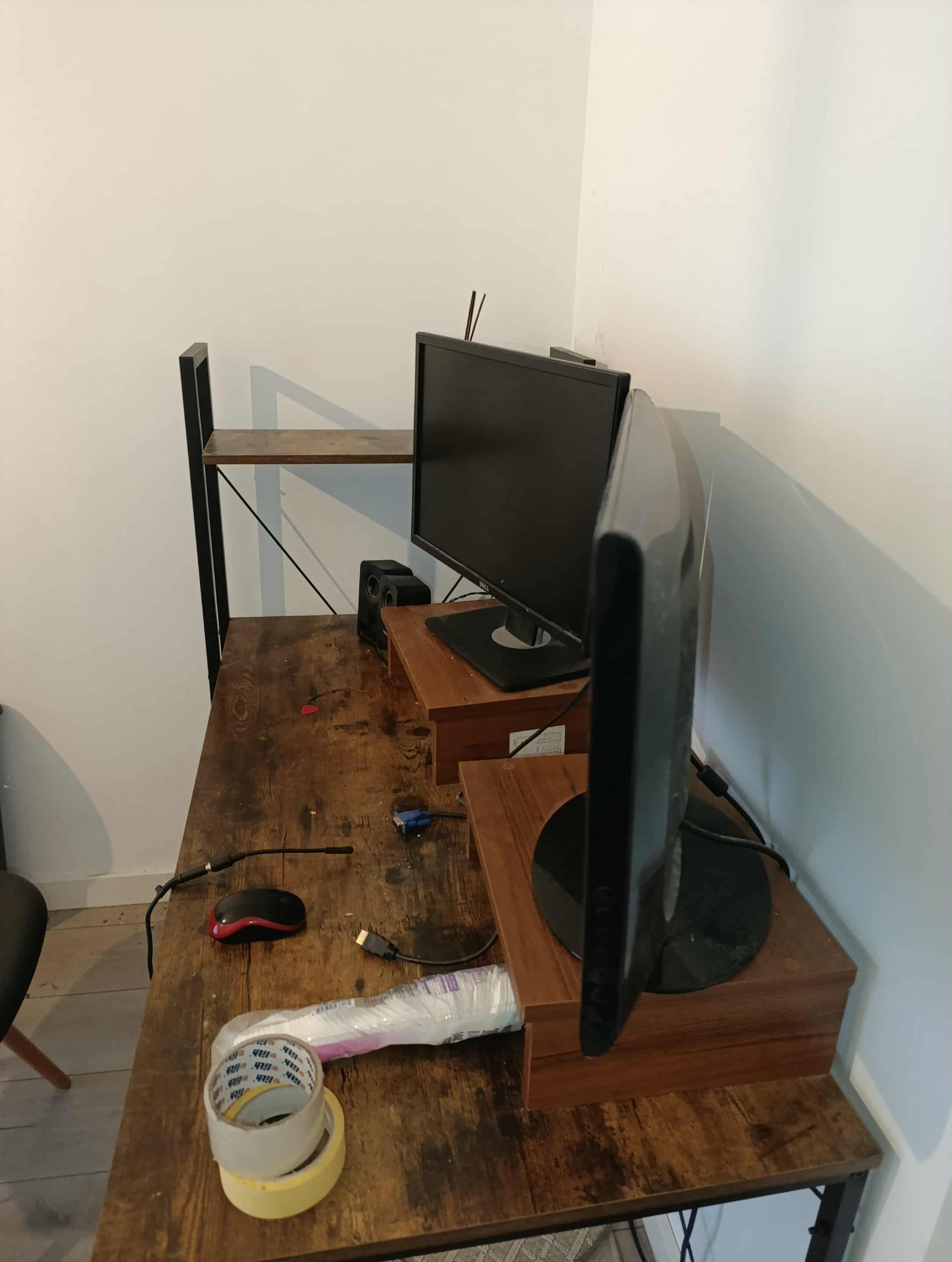 Brudne biurko z dwoma monitorami, myszką, kablami i taśmą klejącą. Widok z góry na nieporządek na biurku.