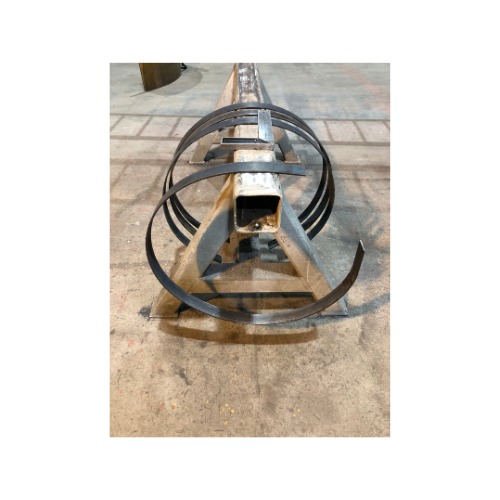 Metalowa konstrukcja z trzema okręgami z płaskownika, ustawiona na podłodze hali; widok z bliska, perspektywa z dołu.