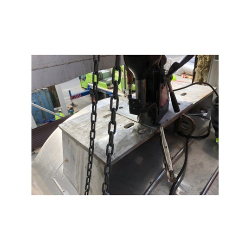 Przenośna wiertarka magnetyczna w trakcie pracy na metalowej konstrukcji. Widoczne łańcuchy zabezpieczające, zaciski i fragmenty spawów. Ujęcie z bliska, robocze otoczenie.