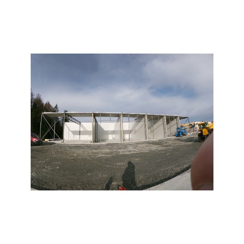 Konstrukcja stalowa hali w trakcie budowy, widoczne elementy spawane, szkielet budynku, maszyny budowlane w tle.