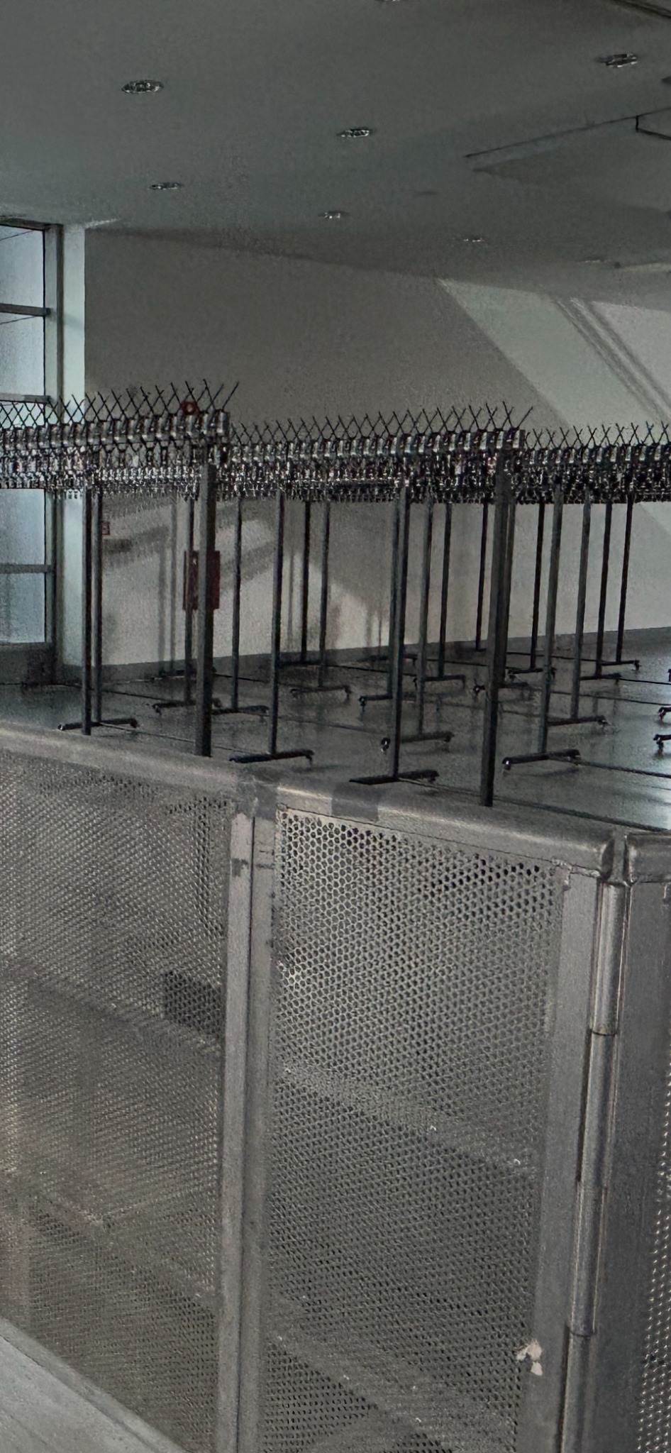 Metalowe bariery i stojaki w magazynie, gotowe do użycia na imprezie. Widoczne oświetlenie sufitowe i okno z lewej strony. Elementy wyposażenia eventowego.