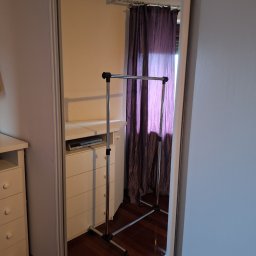 CrystalWave Cleaning - Odbicie w lustrze ukazuje uporządkowane wnętrze pokoju w Warszawie. Widoczna komoda, wieszak na ubrania i zasłony, co sugeruje dbałość o detale i czystość.
