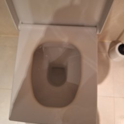 CrystalWave Cleaning - Czysta, kwadratowa toaleta z otwartą klapą, widok z góry. Jasne płytki podłogowe i uchwyt na papier toaletowy w tle. Minimalistyczny design łazienki po sprzątaniu.