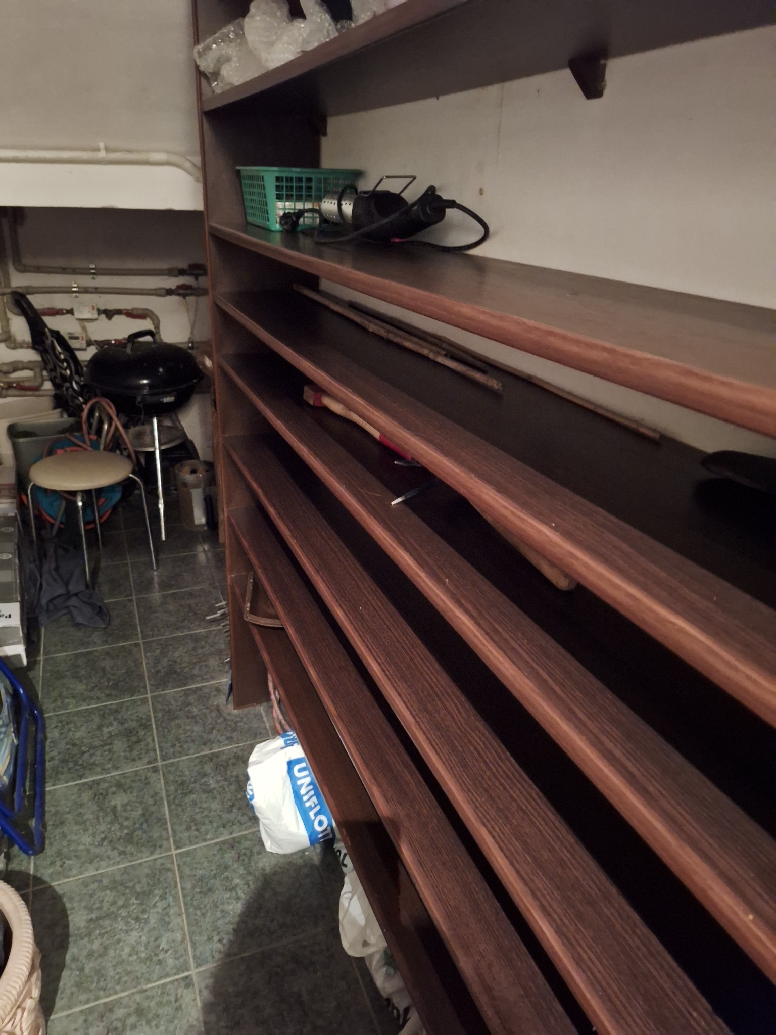 Półki z ciemnego drewna w pomieszczeniu z grillem, narzędziami i workiem. Widok z dołu, ukazujący nieporządek i potrzebę posprzątania.