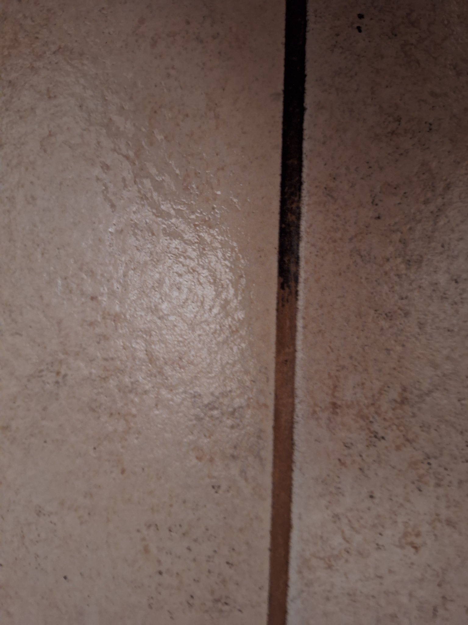 Brudna fuga między beżowymi płytkami podłogowymi. Widoczne zabrudzenia i plamy na powierzchni płytek. Niejednolita kolorystyka fugi.