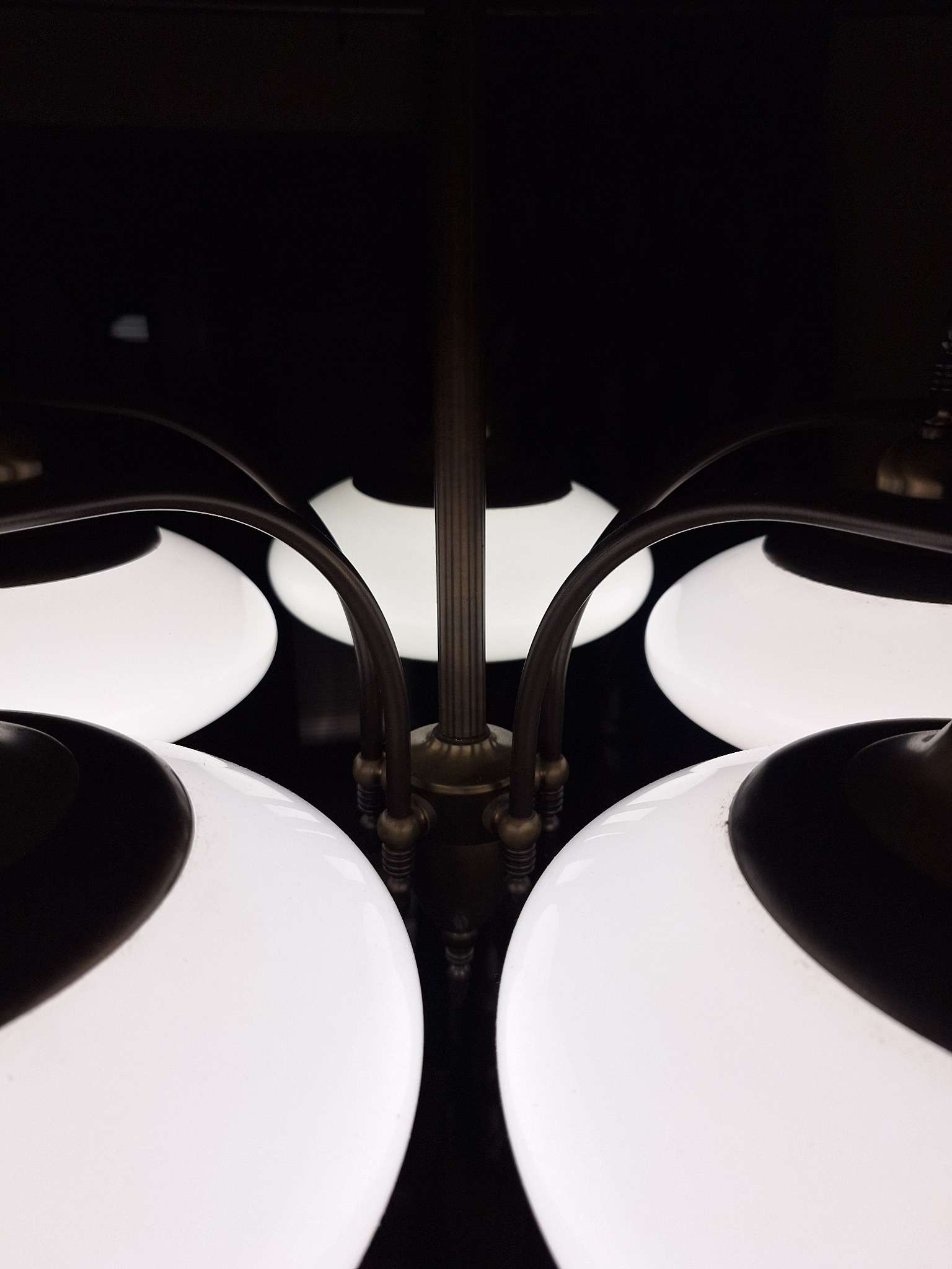 Żyrandol z białymi, kulistymi kloszami i metalową konstrukcją w ciemnym otoczeniu. Ujęcie z dołu, podkreślające symetrię i detale wykończenia.