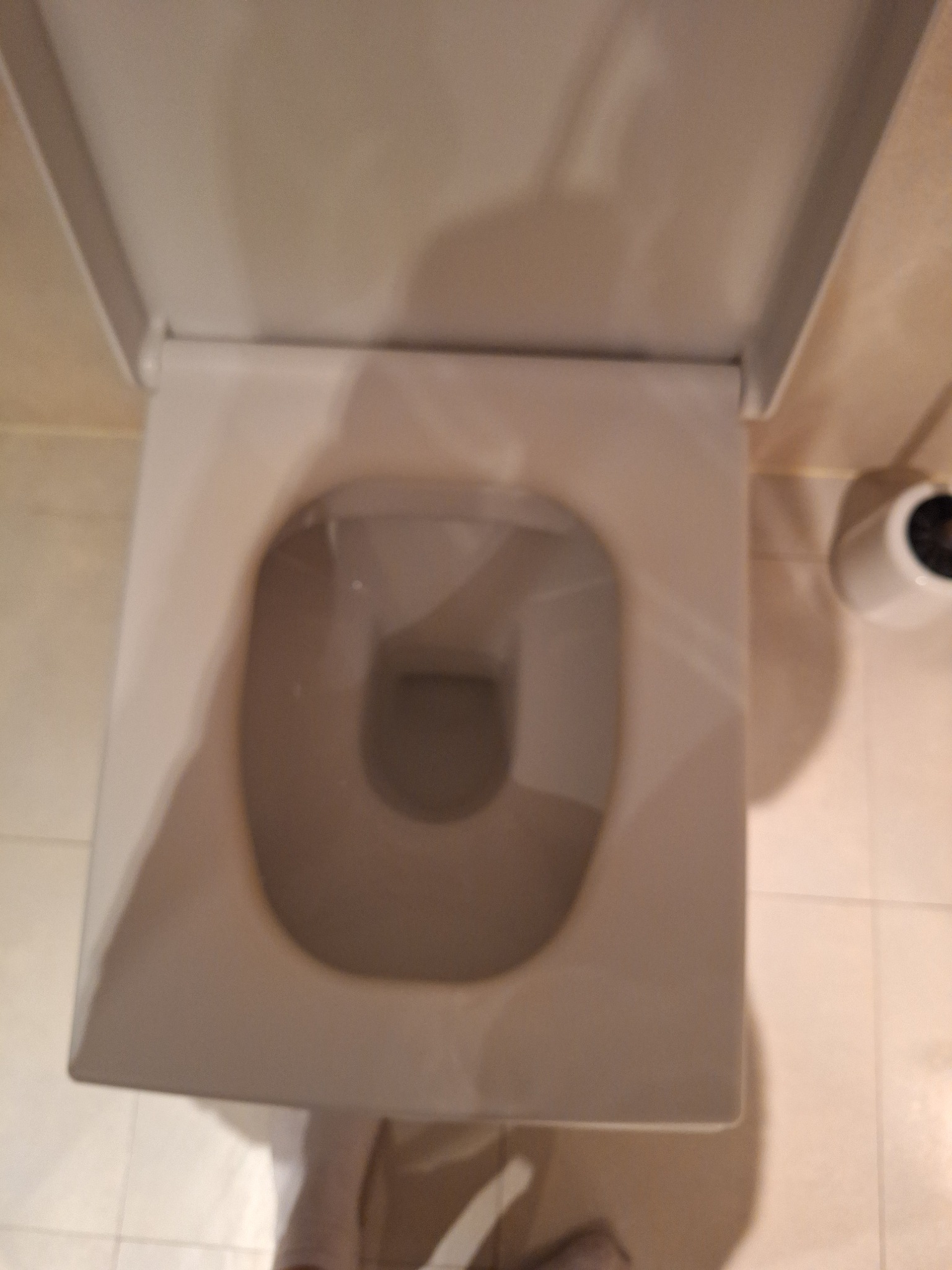 Czysta, kwadratowa toaleta z otwartą klapą, widok z góry. Jasne płytki podłogowe i uchwyt na papier toaletowy w tle. Minimalistyczny design łazienki po sprzątaniu.