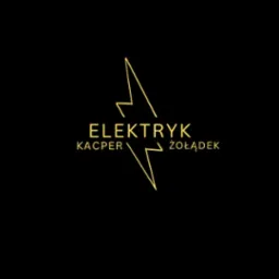 Złoty logotyp firmy elektrycznej na czarnym tle. Stylizowany symbol błyskawicy, nazwa firmy 'ELEKTRYK Kacper Żołądek'. Minimalistyczny design, nowoczesny charakter.