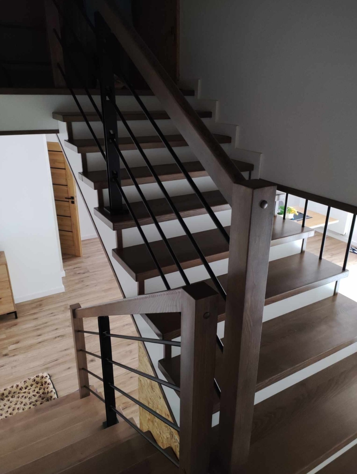 Nowoczesne schody drewniane z czarnymi, metalowymi balustradami. Widok z góry, ukazujący detale wykończenia i jasną kolorystykę wnętrza.