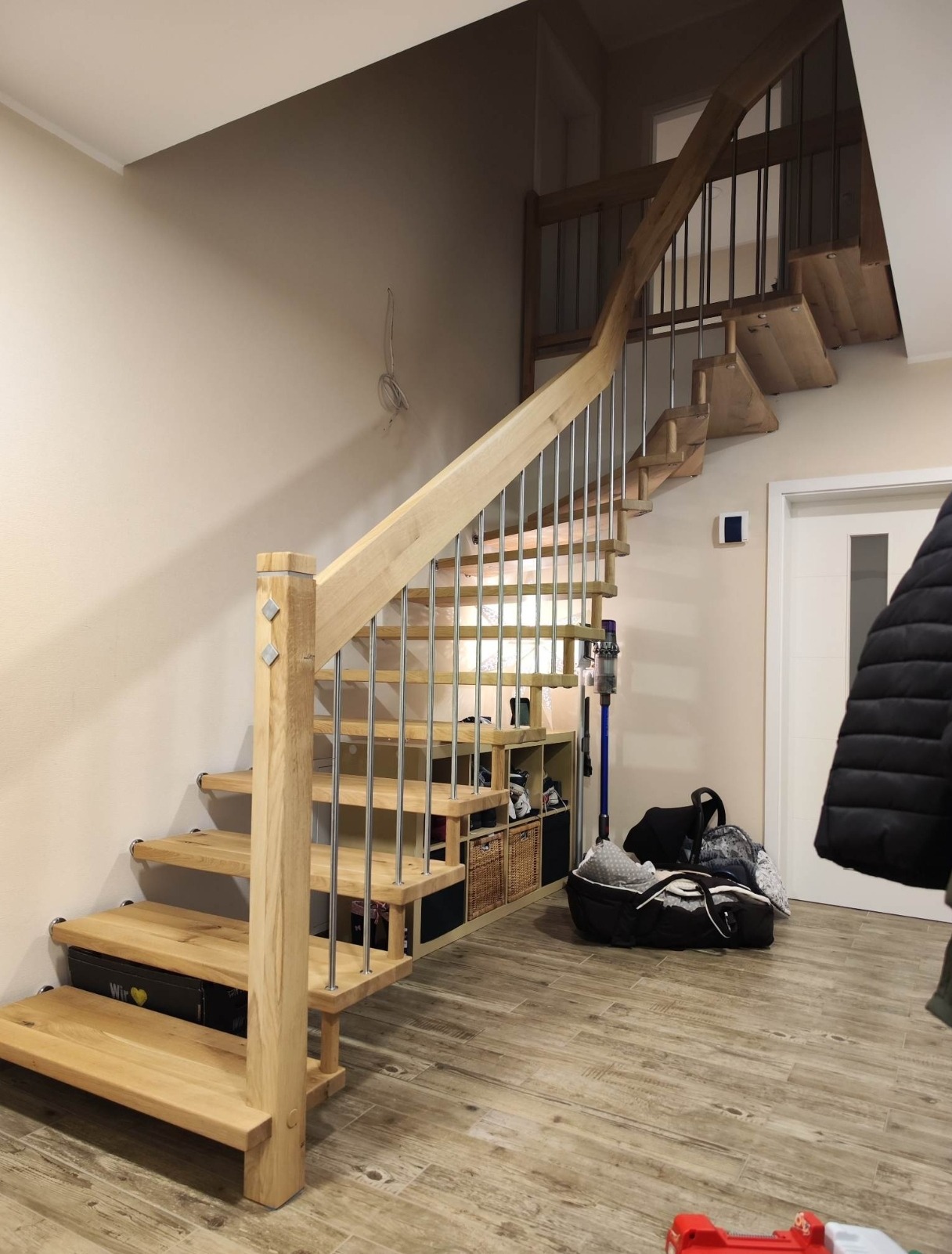 Drewniane schody z metalowymi barierkami w jasnym wnętrzu. Widoczne półki pod schodami i elementy wykończenia. Ujęcie z dołu, podkreślające konstrukcję.