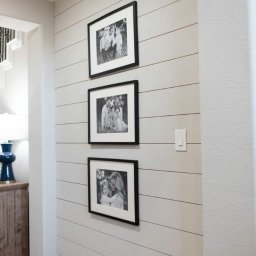 Kossako adrian kossakowski - Szara ściana z desek, na której wiszą trzy czarno-białe zdjęcia w czarnych ramkach. Widoczny fragment korytarza i schodów.