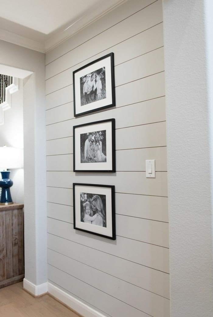Szara ściana z desek, na której wiszą trzy czarno-białe zdjęcia w czarnych ramkach. Widoczny fragment korytarza i schodów.