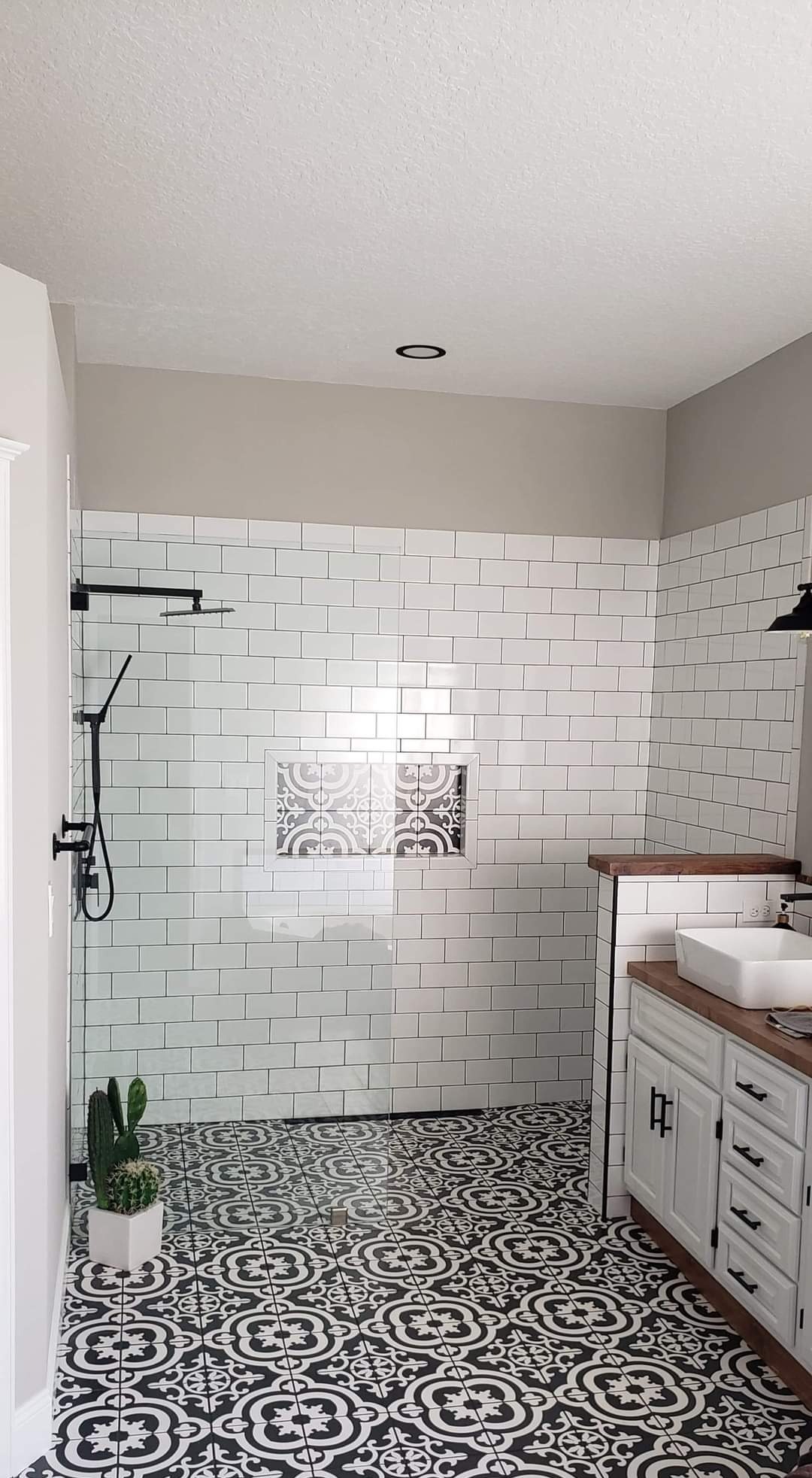 Nowoczesna łazienka z białą armaturą, geometryczną posadzką i kabiną prysznicową wyłożoną białymi płytkami. Wnęka z dekoracyjnym wzorem.