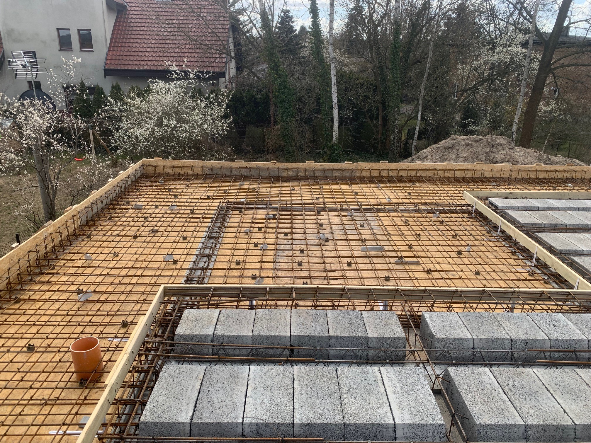 Zbrojenie stropu budynku z szalunkiem i pustakami stropowymi. Widok z góry na przygotowaną konstrukcję przed zalaniem betonem, z elementami drewnianymi i stalowymi.