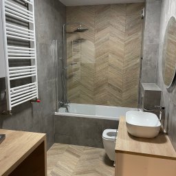 Wojciech Siemaszko - Nowoczesna łazienka z szarymi płytkami i drewnopodobną mozaiką na ścianie, biała umywalka nablatowa i grzejnik drabinkowy.