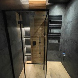 Wojciech Siemaszko - Nowoczesna łazienka z kabiną prysznicową walk-in, drewnianymi akcentami i grafitowymi płytkami. Minimalistyczny design, oświetlenie LED i grzejnik drabinkowy.