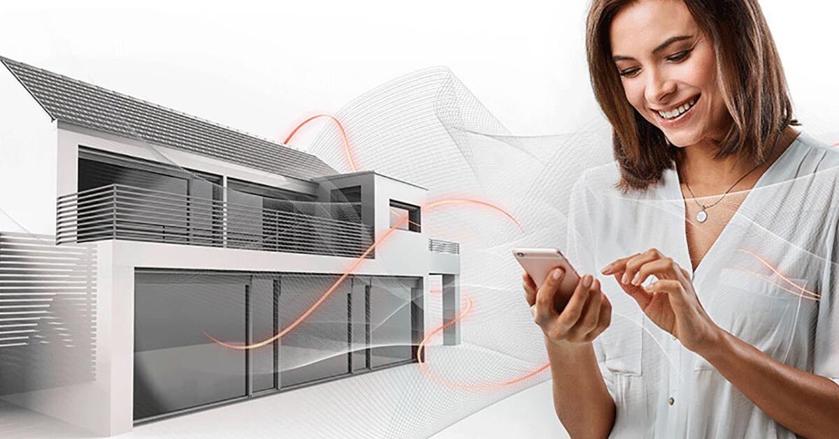 Kobieta uśmiechnięta, korzysta z aplikacji na smartfonie na tle nowoczesnego domu z instalacją grzewczą, wizualizacja przepływu ciepła.